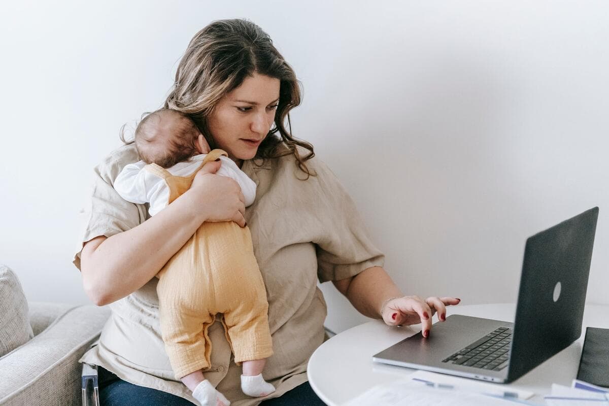 Mulher segurando um bebê recém-nascido enquanto trabalha no notebook em casa