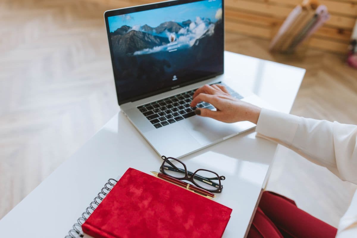 Pessoa trabalhando em um laptop em uma mesa de home office com nobreak ao lado.