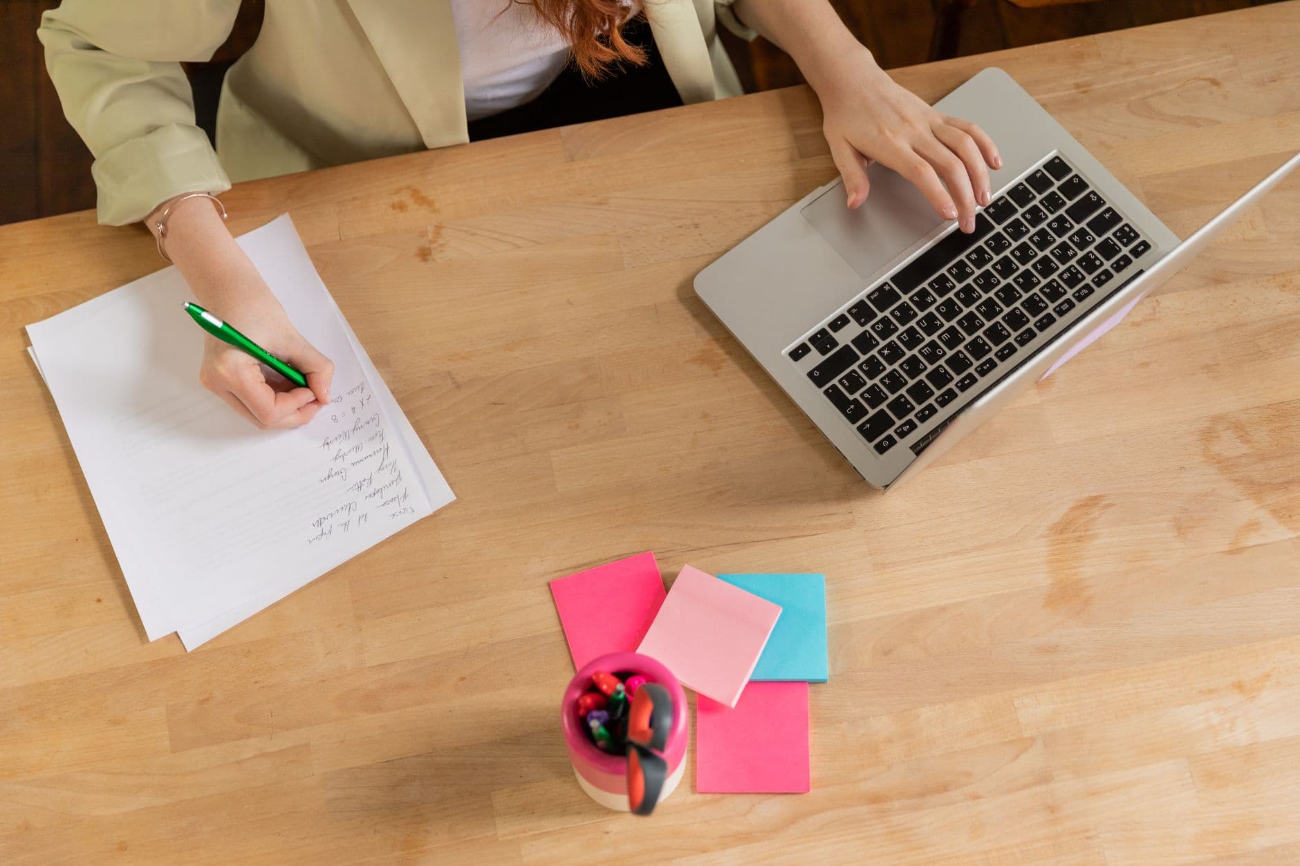 Pessoa trabalhando em um laptop com páginas organizadas em uma mesa de home office