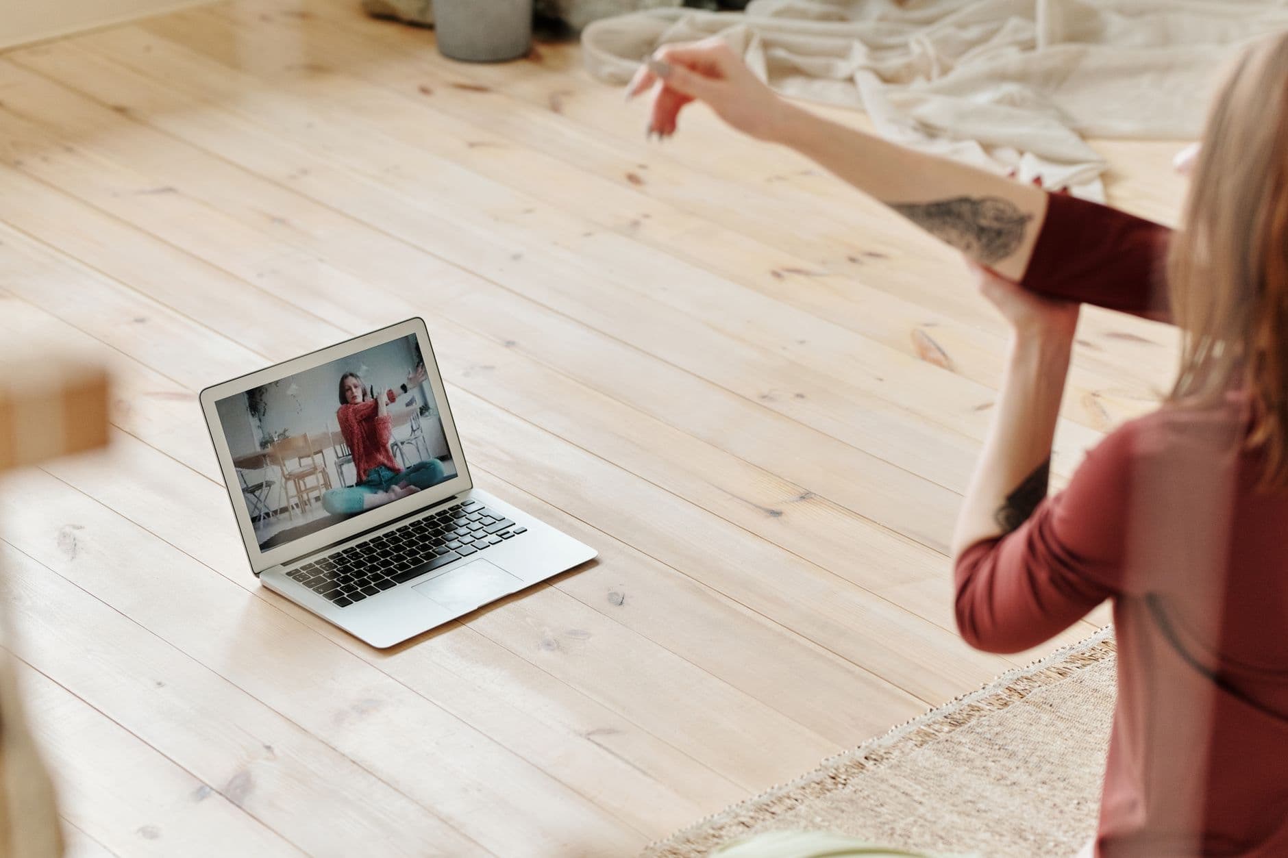 Por que fazer pausas durante o trabalho remoto A woman stretches while following an online yoga class on a laptop in a cozy indoor setting.
