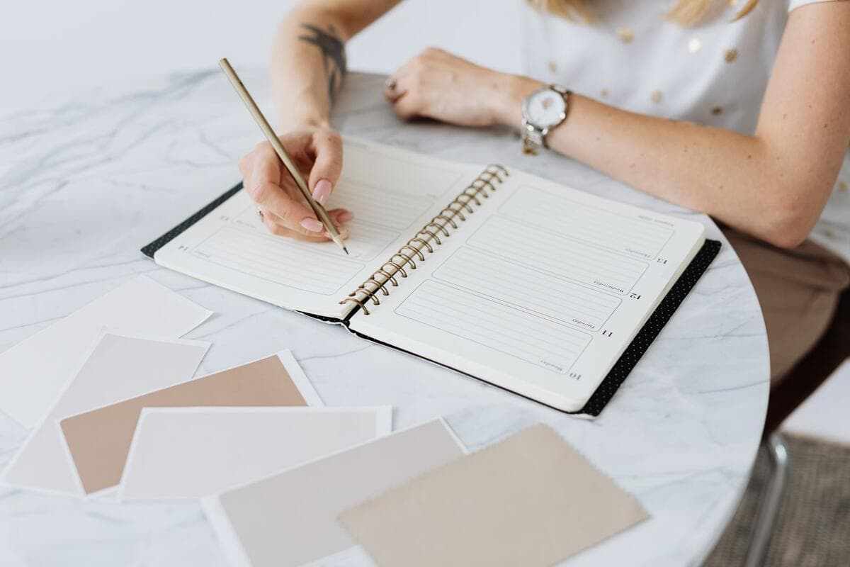 O que a empresa avalia em quem trabalha remoto Mulher escrevendo em uma agenda sobre uma mesa de mármore