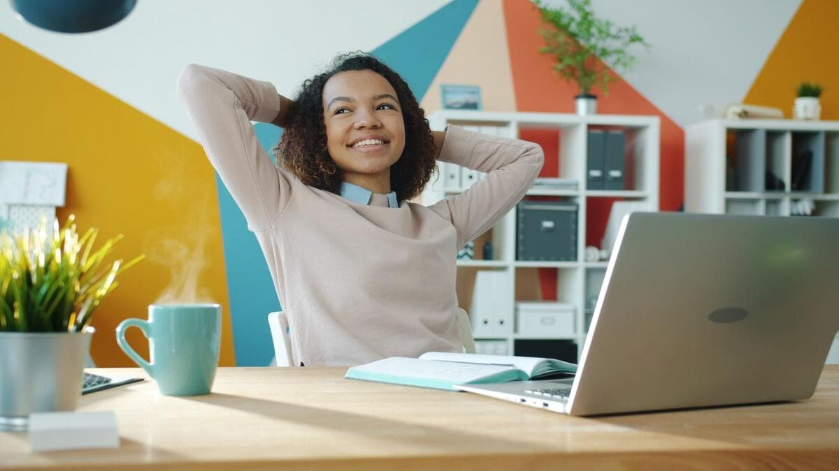 Mulher sorrindo e relaxando diante do notebook em um escritório colorido