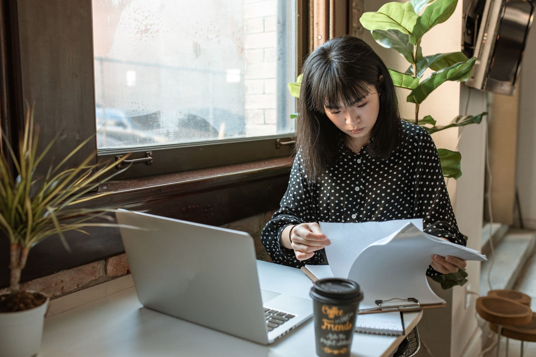 Plataformas para freelancer iniciante começar a trabalhar Asian businesswoman reviewing documents in a modern office setting with natural light.
