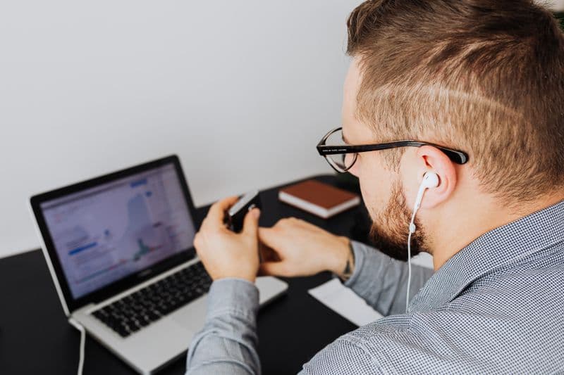 Ponto eletrônico no teletrabalho: como funciona A business professional uses a laptop with charts and graphs while wearing earphones in an office setting.