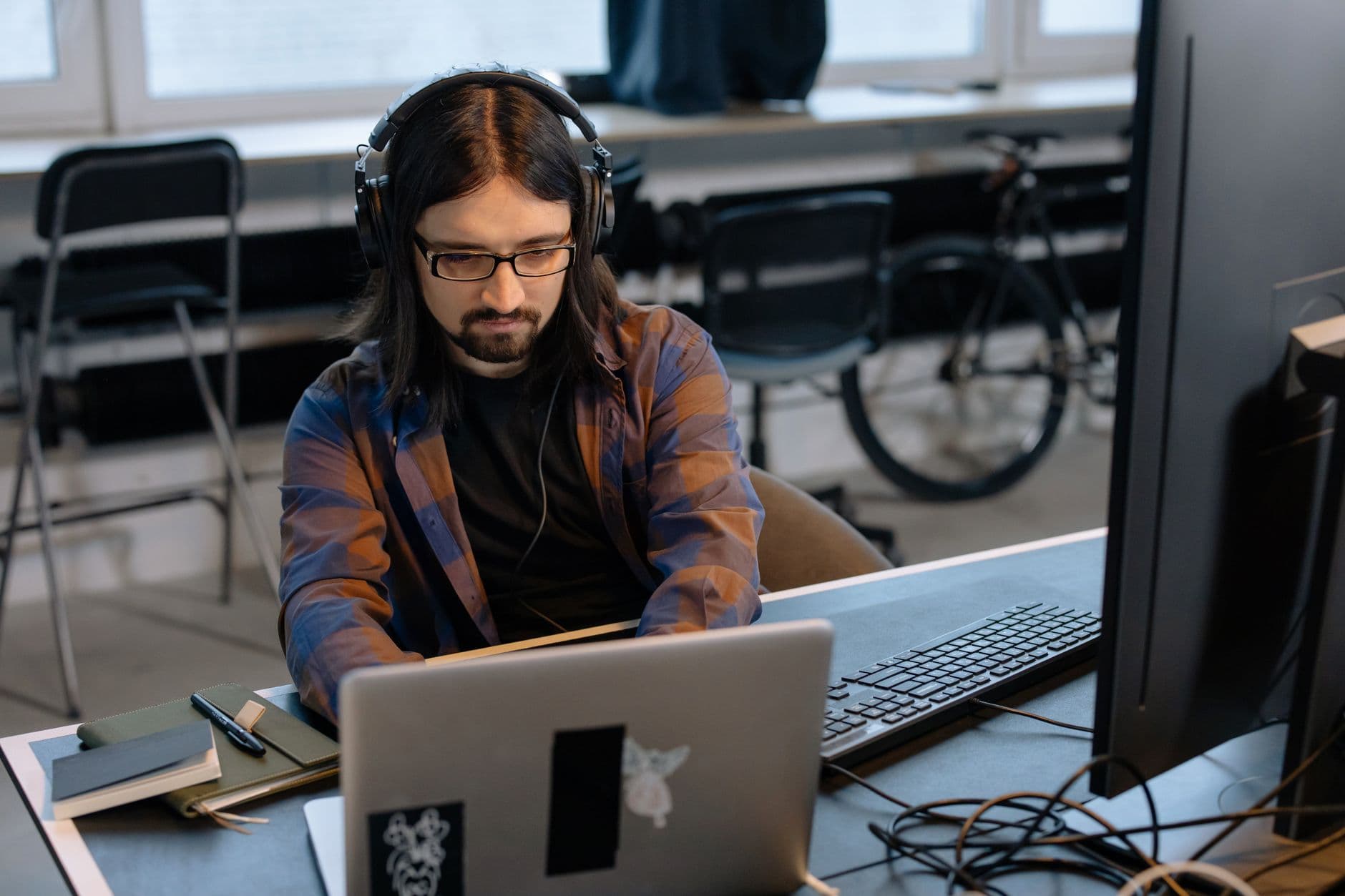 Como usar o GitHub como portfólio para vaga remota Bearded male developer in headphones coding on a laptop in a modern office setting.