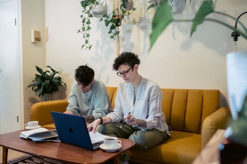 Como fazer uma proposta comercial de freelancer Concentrated young tattooed female freelancers with short dark hair in casual clothes sitting on comfortable sofa and working remotely on laptop