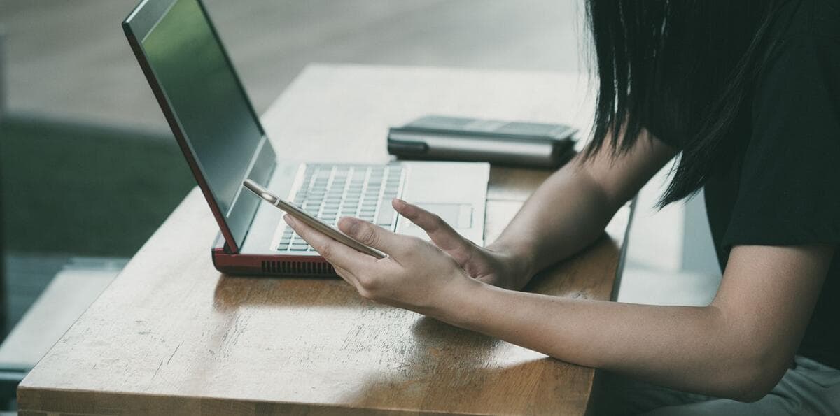 Quanto aumentar Mulher usando celular e notebook ao mesmo tempo em uma mesa
