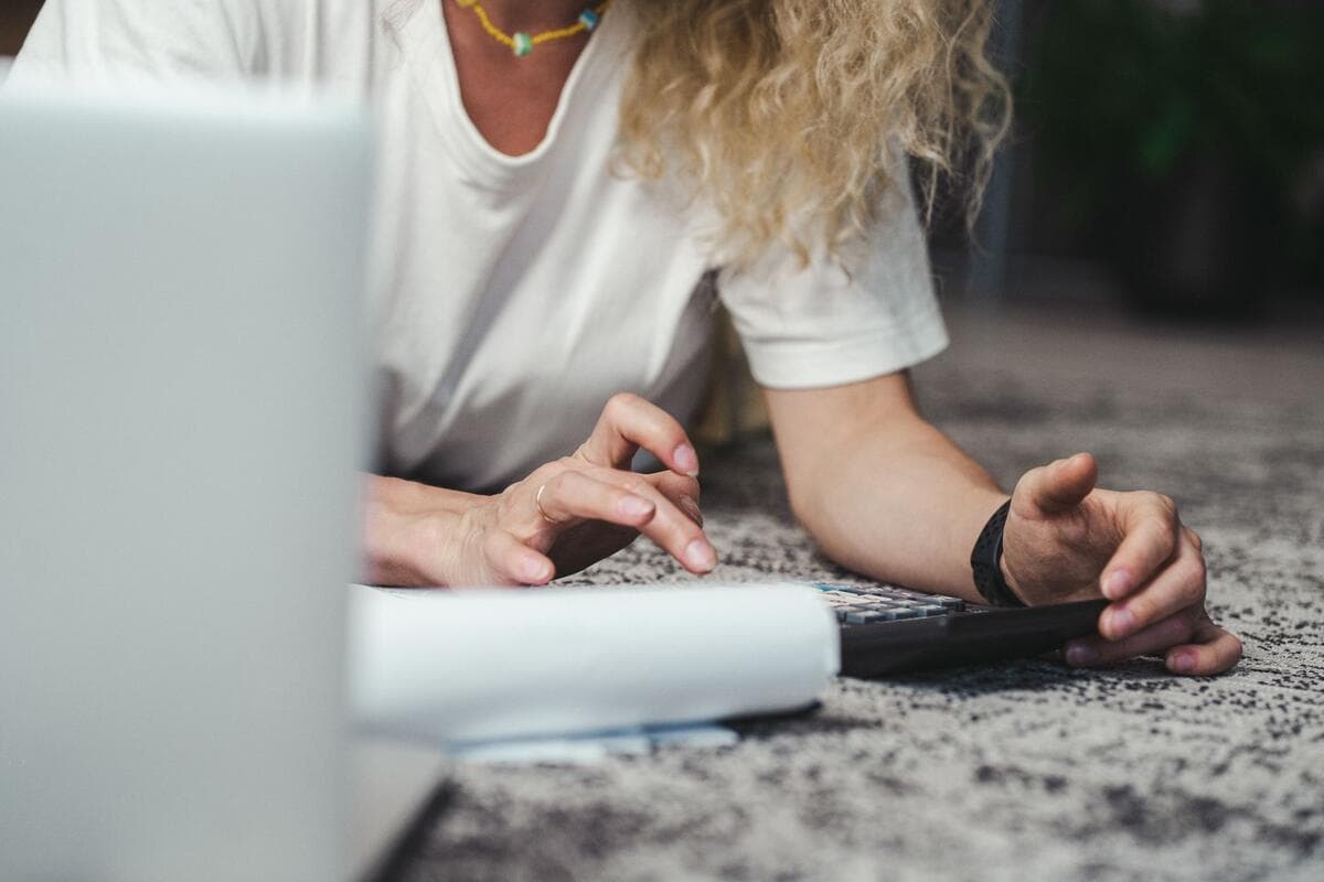 Mulher fazendo contas com calculadora e notebook no chão de casa