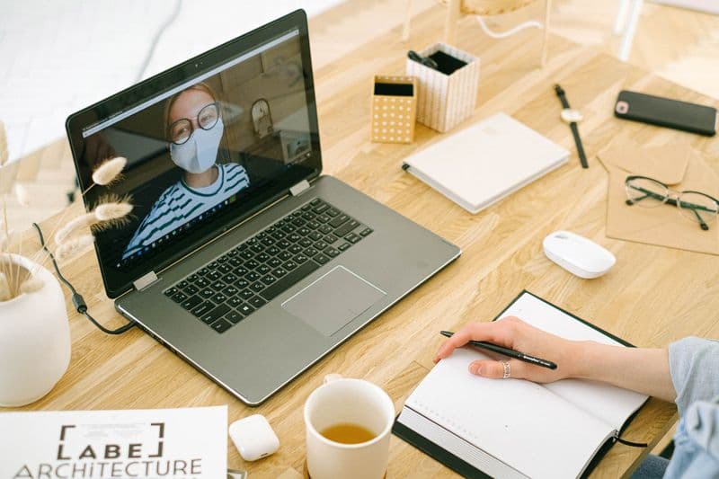 Como conduzir uma reunião individual remota A woman in a home office setup having a video call while taking notes, concept of remote work.