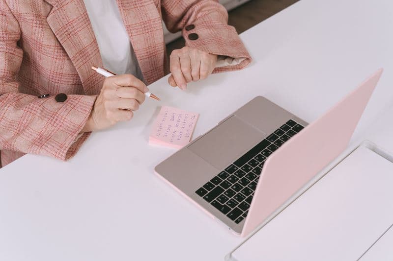 Reunião diária curta: como fazer um stand-up remoto Businesswoman in a plaid jacket using a laptop and sticky notes for work planning.
