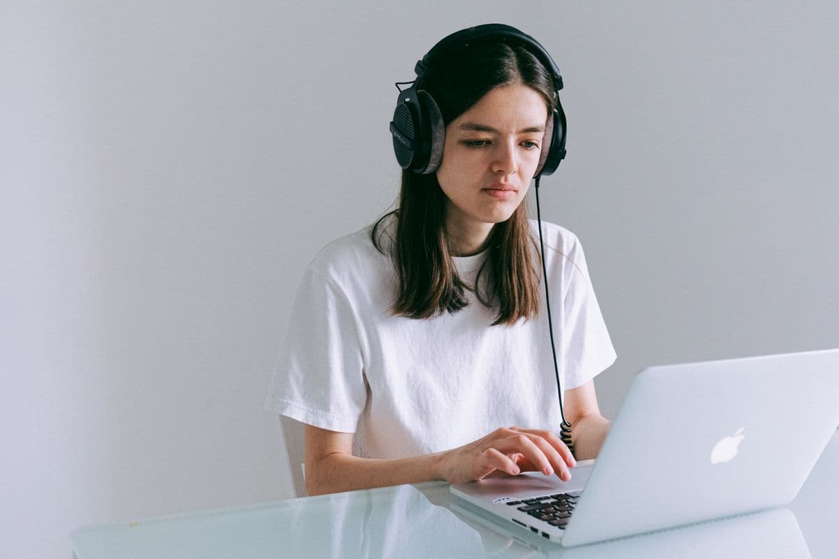 Pessoa trabalhando em um laptop com fones em uma mesa organizada de home office