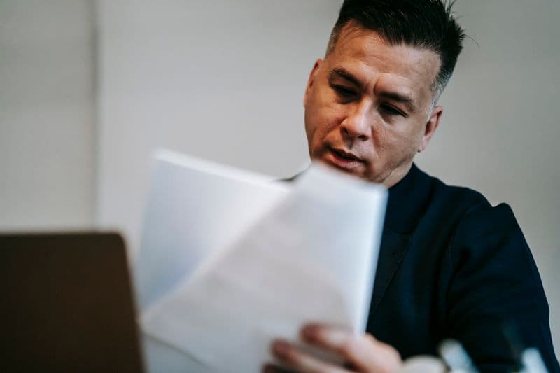 Seguro de vida para quem trabalha em casa vale a pena? Professional man intently reviewing paperwork at his workstation indoors.