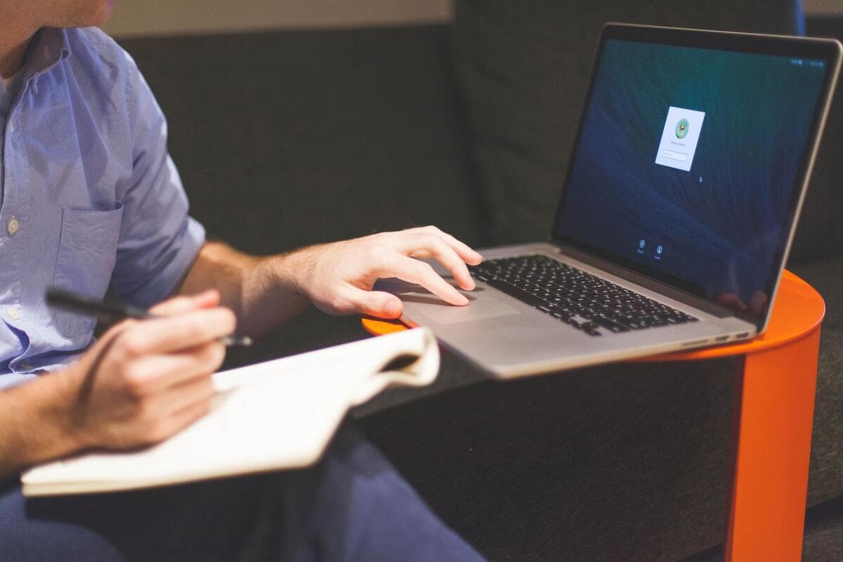 Profissional escrevendo anotações ao lado do notebook enquanto prepara o status report da semana