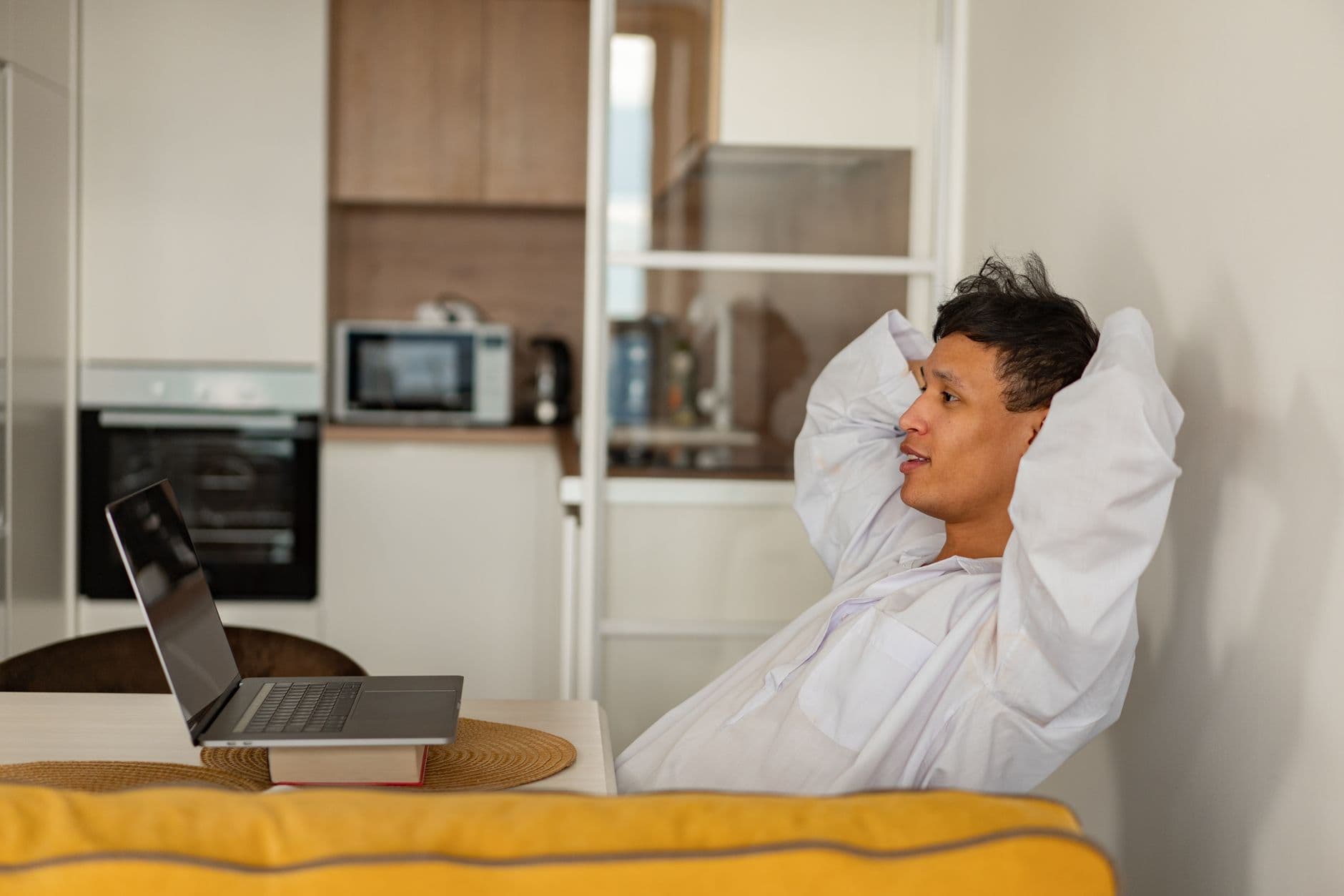 Técnica pomodoro no home office: como aplicar A man in a white shirt relaxes with a laptop in a contemporary kitchen environment, enjoying leisure time.