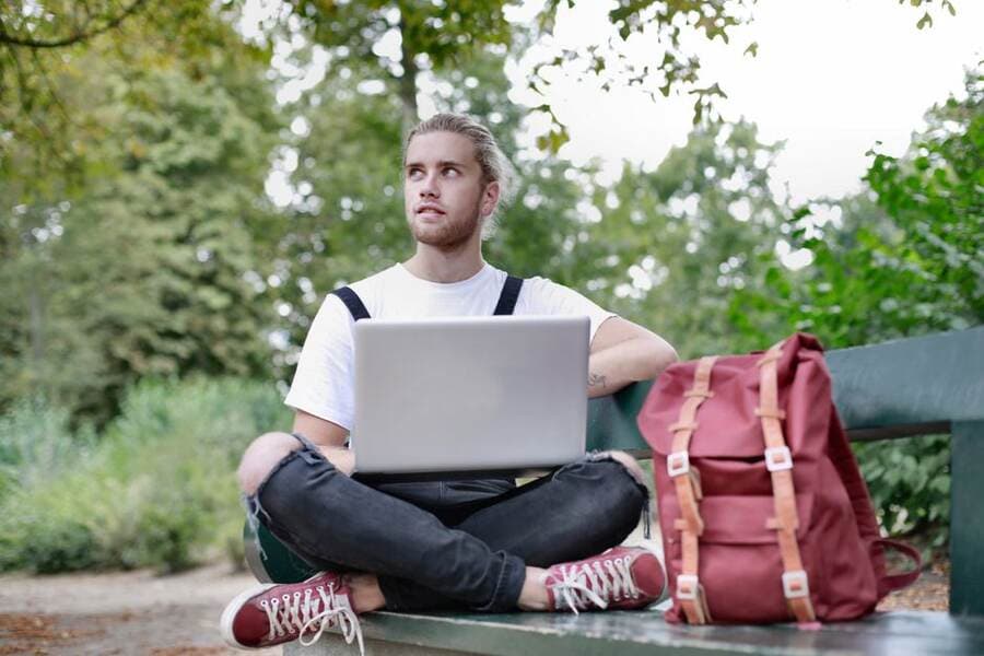 Homem com mochila trabalhando no notebook ao ar livre Homem com mochila trabalhando no notebook ao ar livre