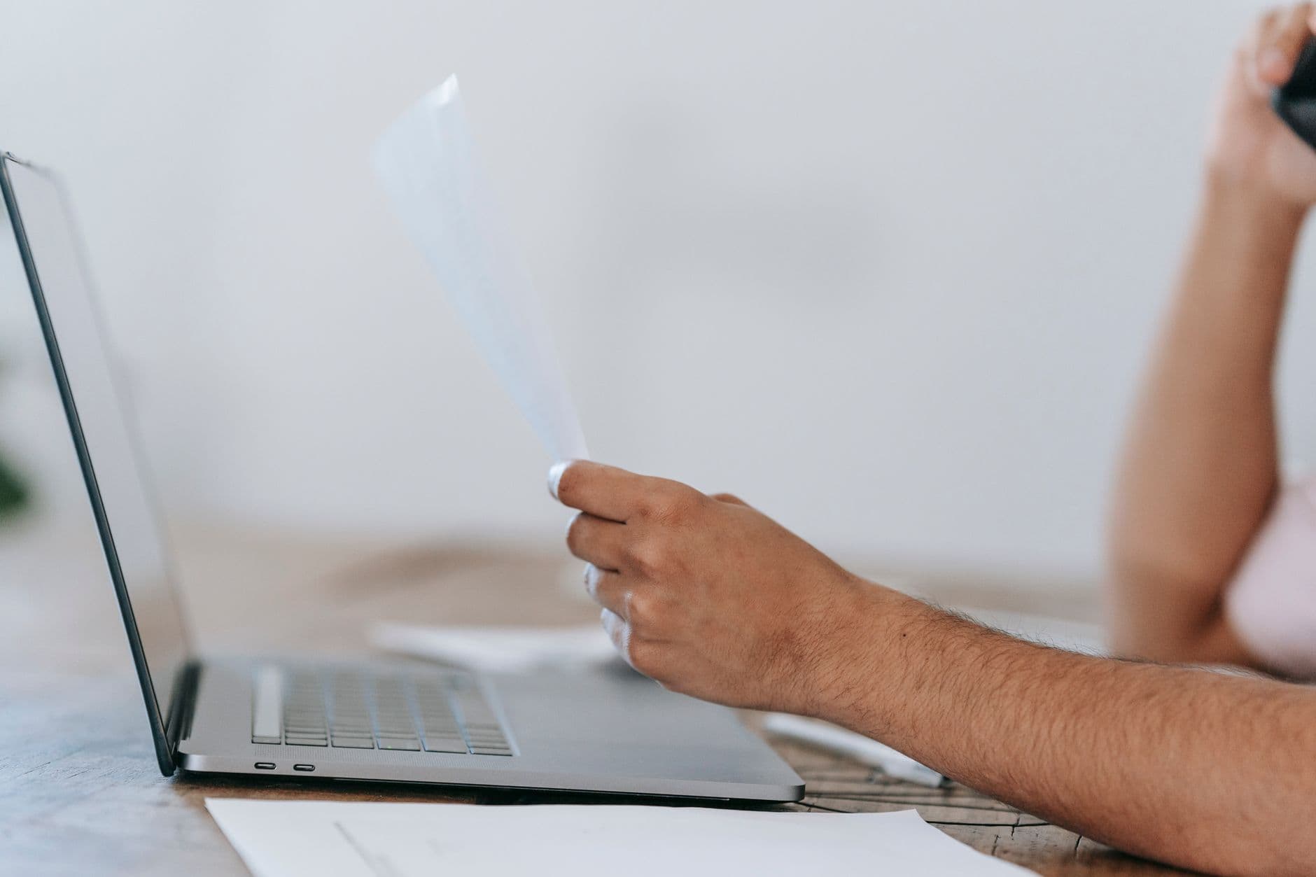 Upwork: como começar do zero Crop anonymous male reading document and talking on mobile phone while sitting at desk with laptop
