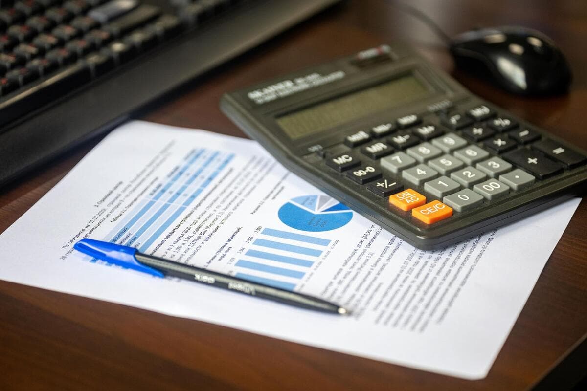 O que os escritórios pedem de quem trabalha a distância Calculadora, relatório financeiro e caneta sobre uma mesa de trabalho