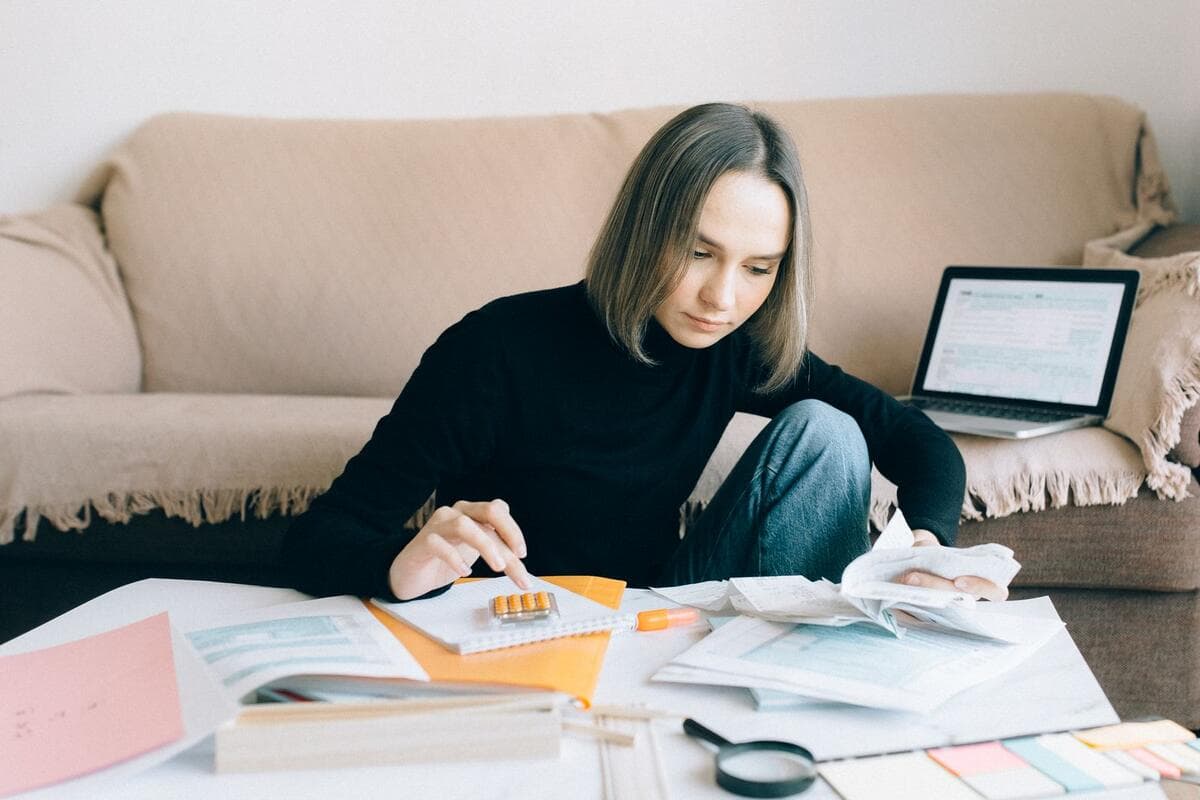 Mulher organizando documentos financeiros e usando notebook na sala de casa