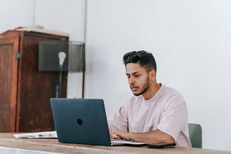 Moderador de conteúdo remoto: rotina e cuidados Concentrated young ethnic male distance employee with modern haircut working on netbook while sitting at desk