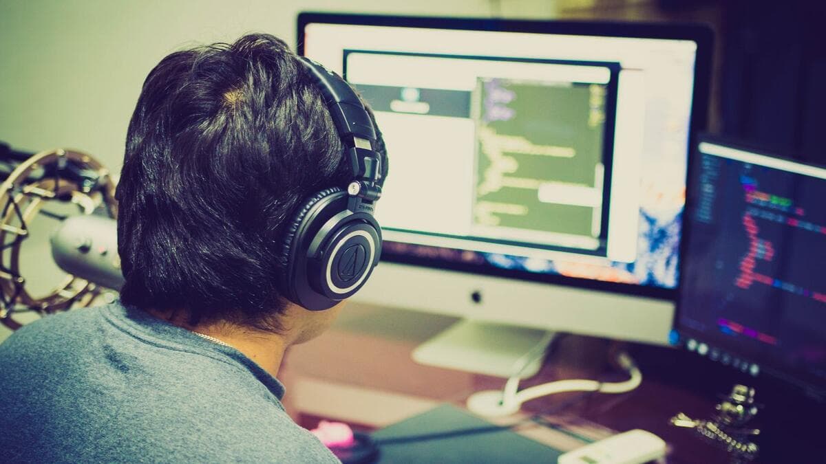 O que estudar, e em qual ordem Programador com fones de ouvido trabalhando em dois monitores