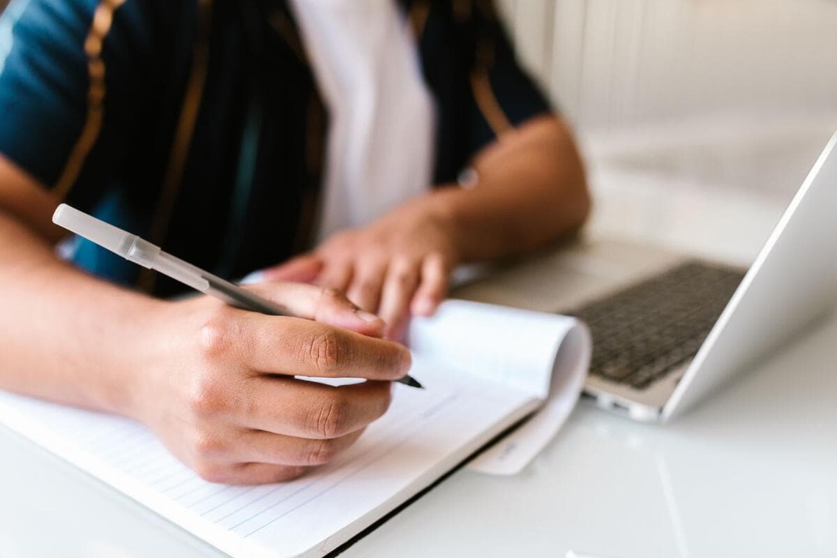 Onde encontrar vagas remotas de QA Pessoa fazendo anotações em um caderno ao lado do notebook
