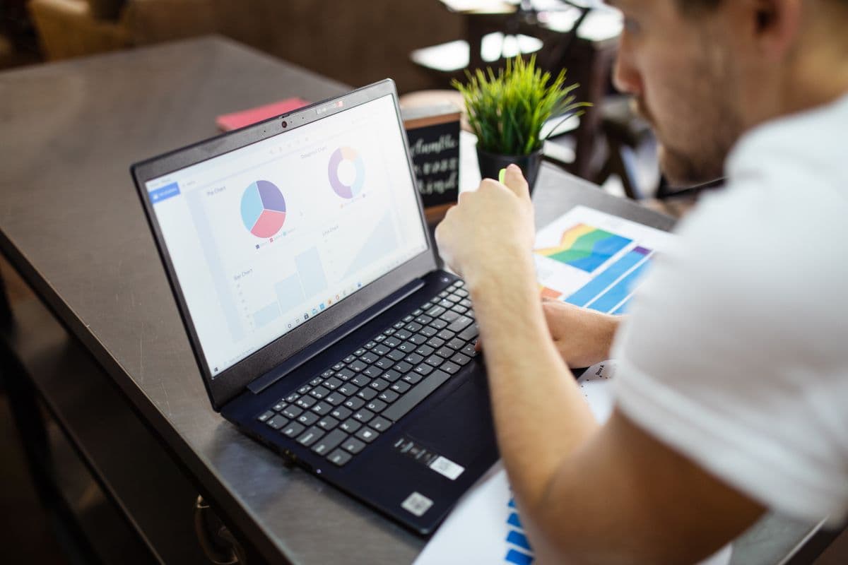 Profissional trabalhando em laptop em um home office com gráficos financeiros na tela