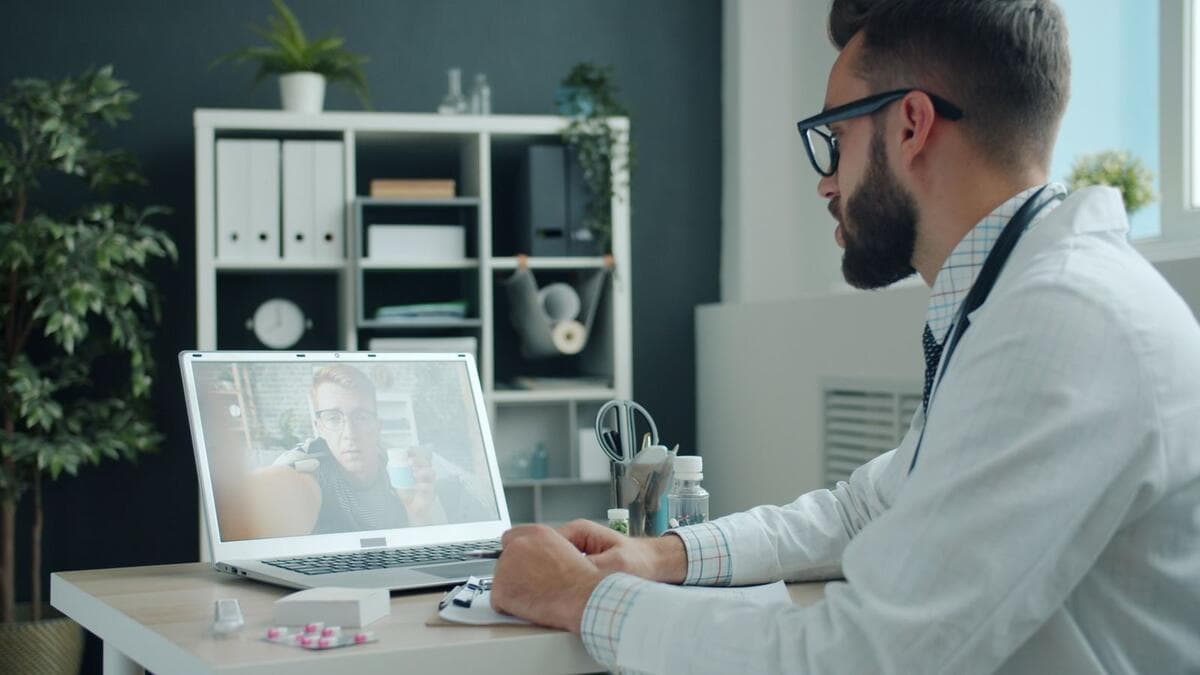 Médico de jaleco branco fazendo teleconsulta com paciente pelo notebook