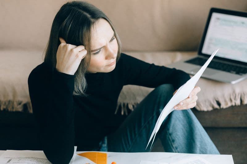 Analista financeiro remoto júnior: vagas e requisitos Focused woman analyzing papers with a laptop open, symbolizing thoughtful consideration.