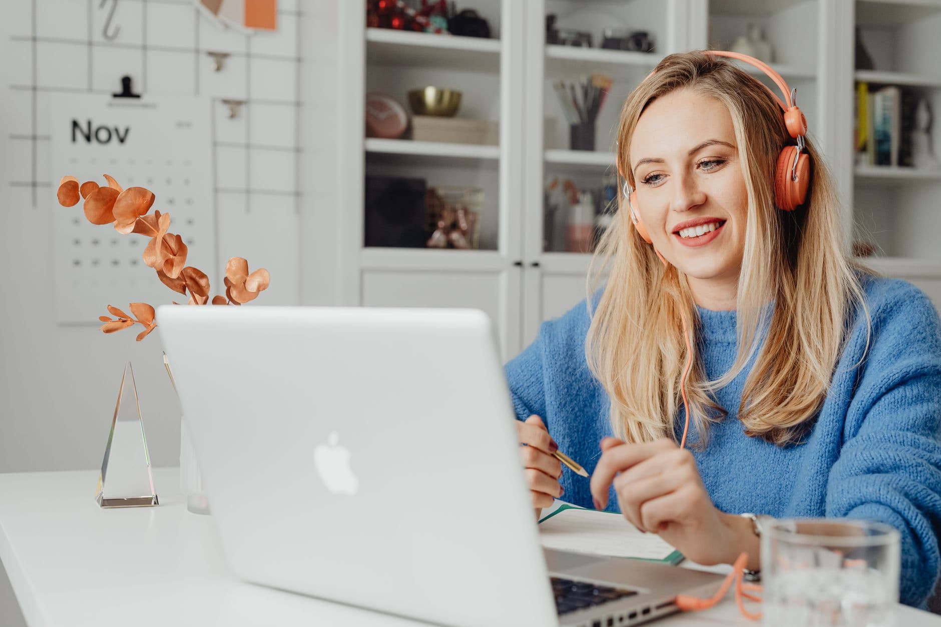 Vagas remotas para atendimento ao cliente: como encontrar Blonde woman smiling while working remotely on a laptop, wearing headphones in a cozy home office.