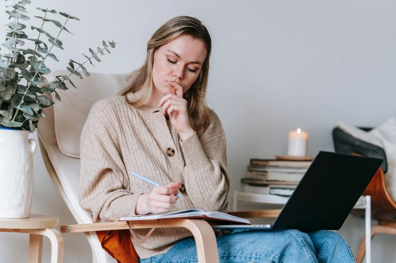 Vagas remotas para copywriter: como conseguir a primeira Pensive young concentrated female freelancing with netbook and diary on armchair in lounge of home
