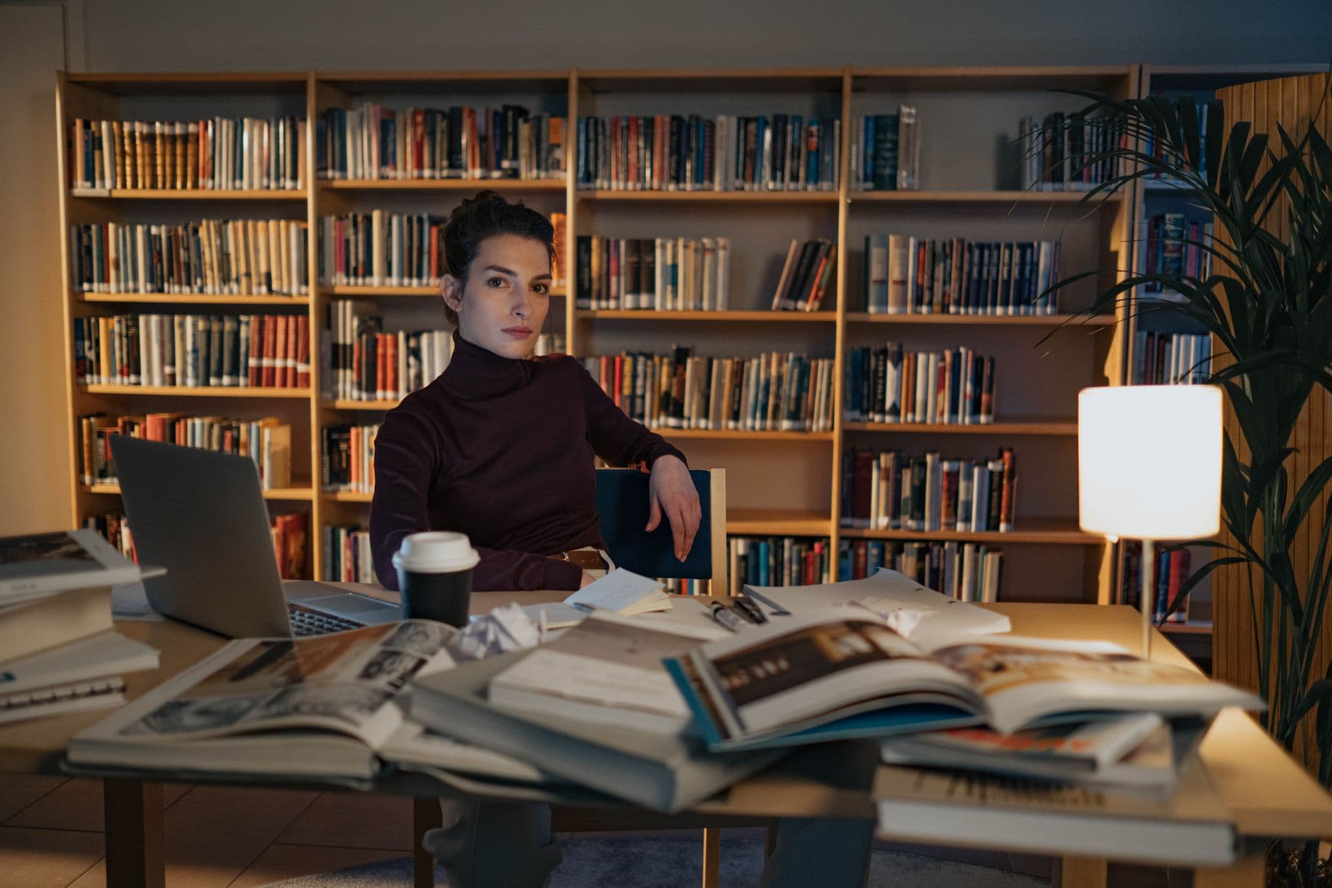 Estudante universitária trabalhando em um laptop ao lado de livros e cadernos em casa.