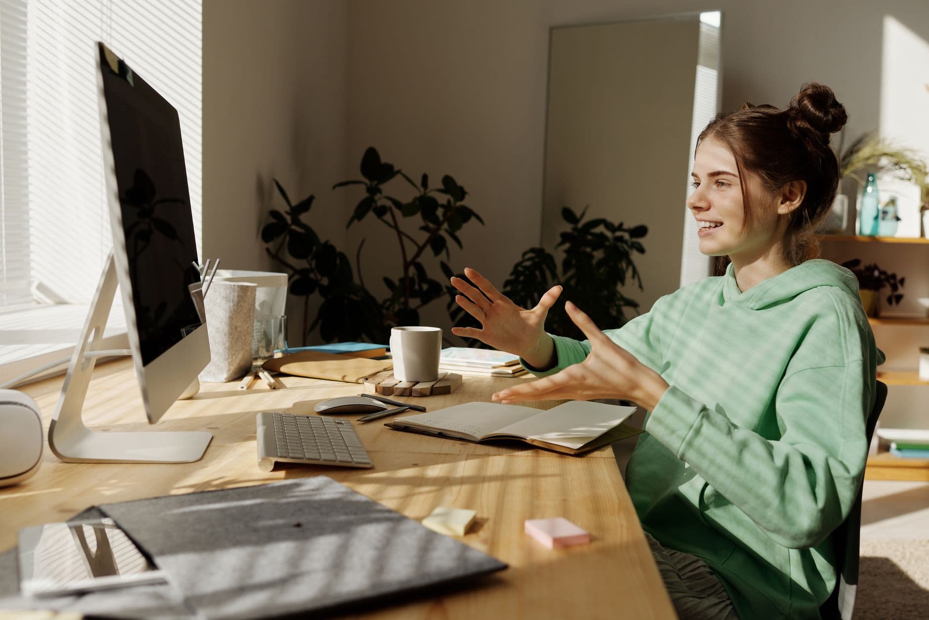 Vagas remotas para estudantes universitários A woman in a green hoodie having a video call at her home office desk.