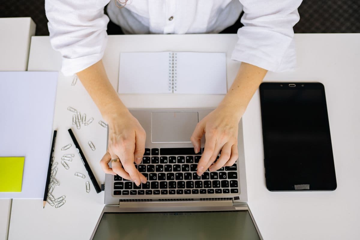 Jornalista trabalhando remotamente em laptop com anotações e gravador sobre a mesa