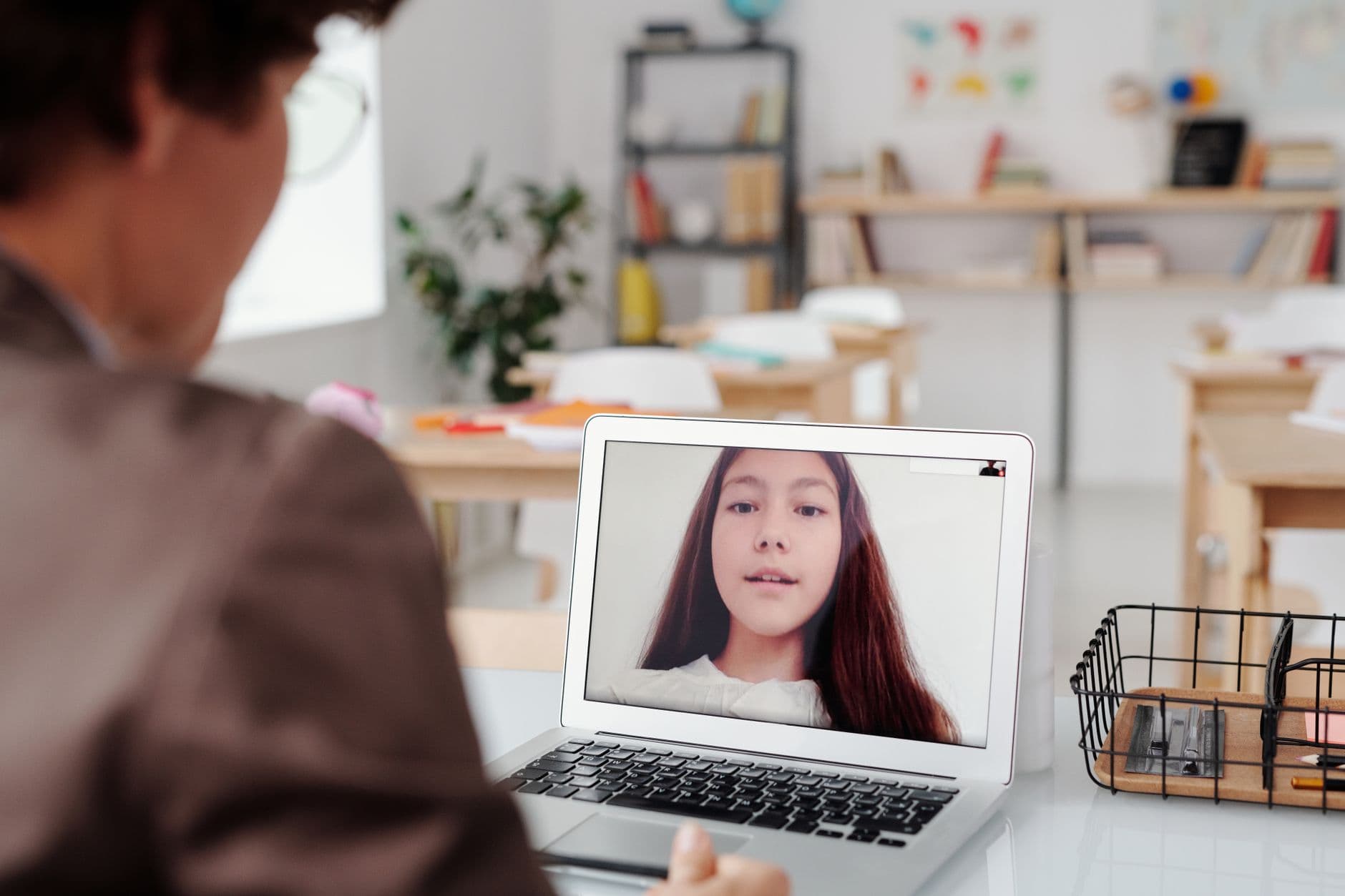 Vagas remotas para professor de idiomas: como encontrar Teacher using laptop for virtual lesson with female student on screen in classroom setting.