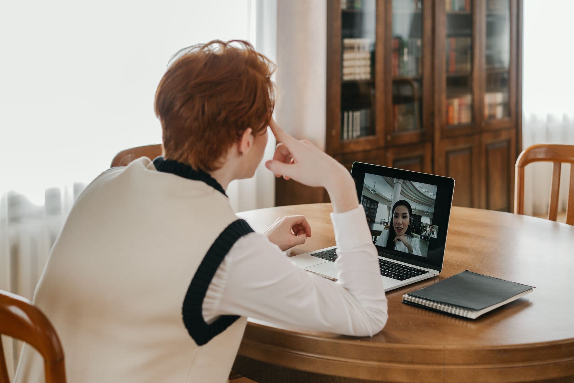 Vagas remotas para quem mora no interior A man sitting at a table, using a laptop for a video call, set in a cozy indoor space.